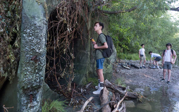 A scene from the movie *It* (2017) featuring Eddie Kaspbrak, portrayed by Wyatt Oleff, exploring a dark entrance while Richie Tozier, played by Finn Wolfhard, and others are in the background.