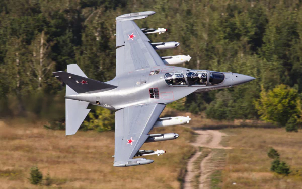 A Yakovlev Yak-130 military jet fighter warplane flies low over a wooded landscape, captured in sharp 4K Ultra HD detail as a PC desktop wallpaper.