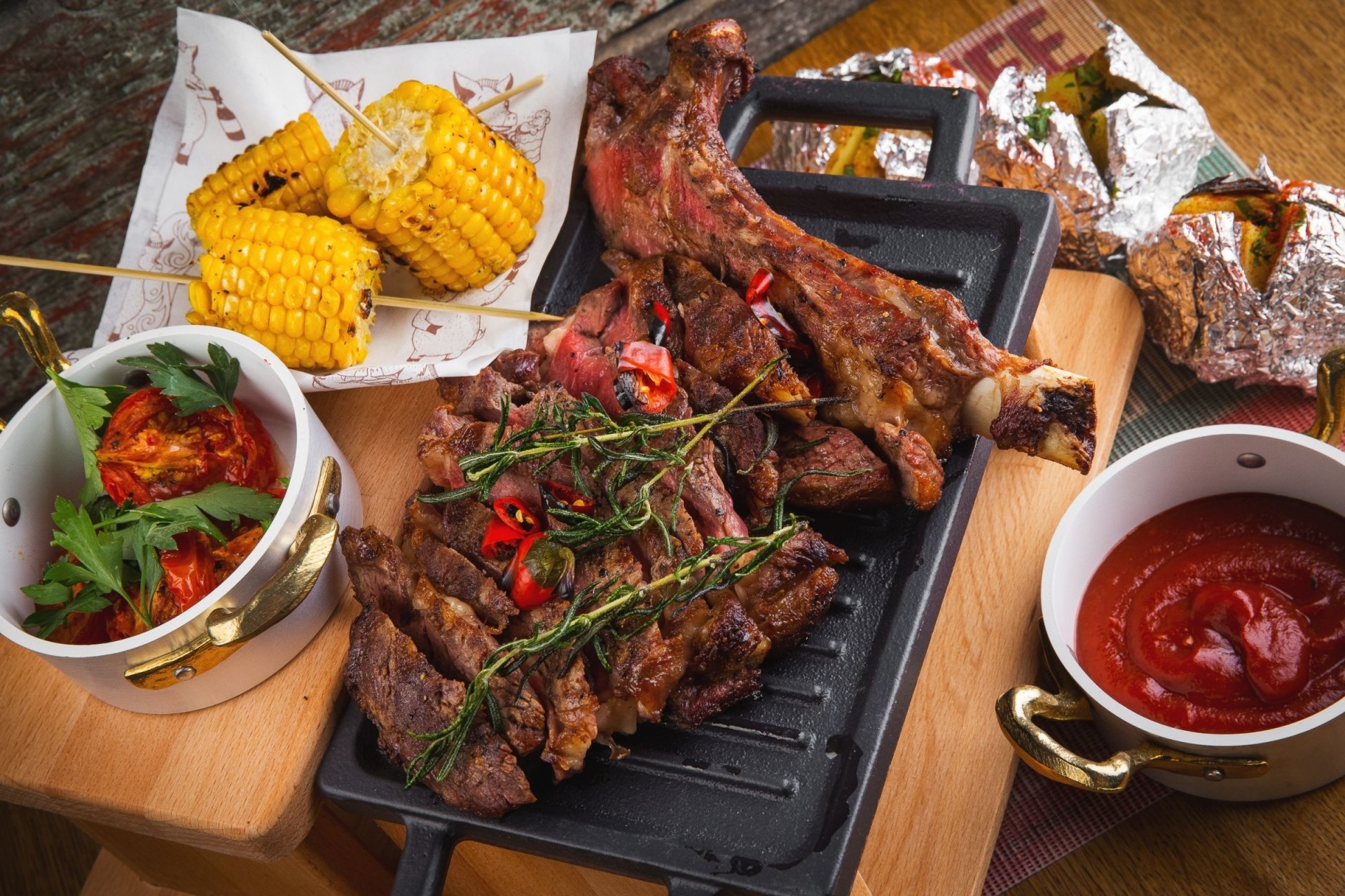 HD desktop wallpaper featuring a vibrant still life of grilled meat, corn on the cob, and a bowl of rich ketchup, showcasing a rustic and hearty food spread.