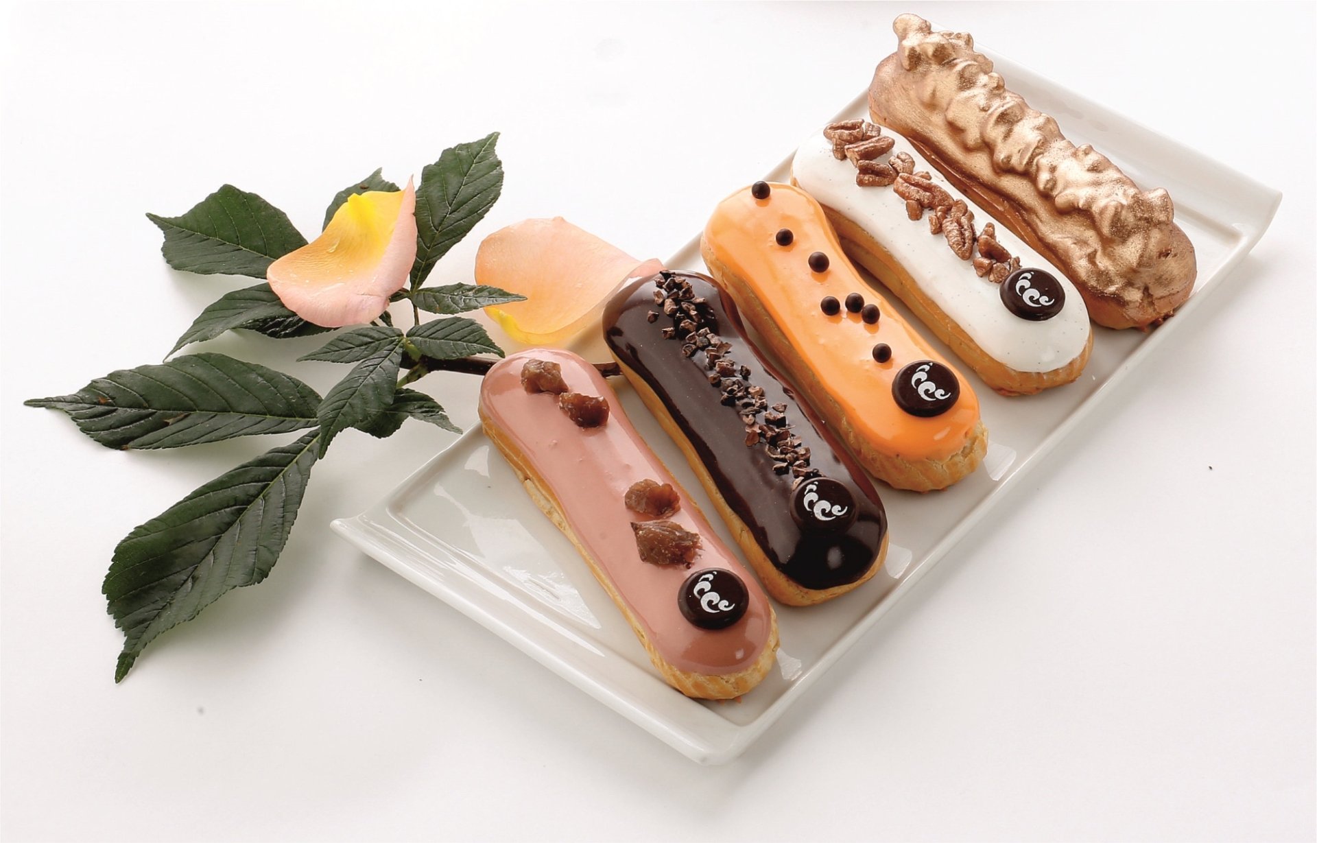 HD PC desktop wallpaper showing five colorful éclair desserts on a glass platter with chocolate garnishes, rose petals and green leaves — food background.