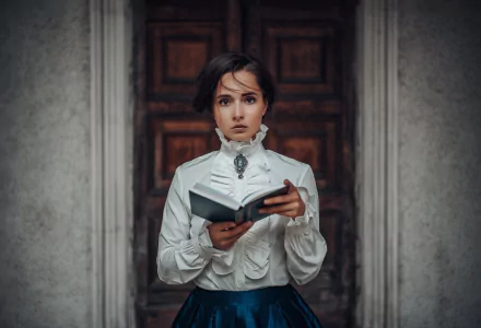 A brunette woman with brown eyes dressed in vintage clothing holds an open book, standing in front of a detailed wooden door, captured as an HD PC desktop wallpaper.