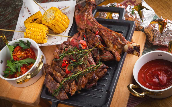 HD desktop wallpaper featuring a vibrant still life of grilled meat, corn on the cob, and a bowl of rich ketchup, showcasing a rustic and hearty food spread.