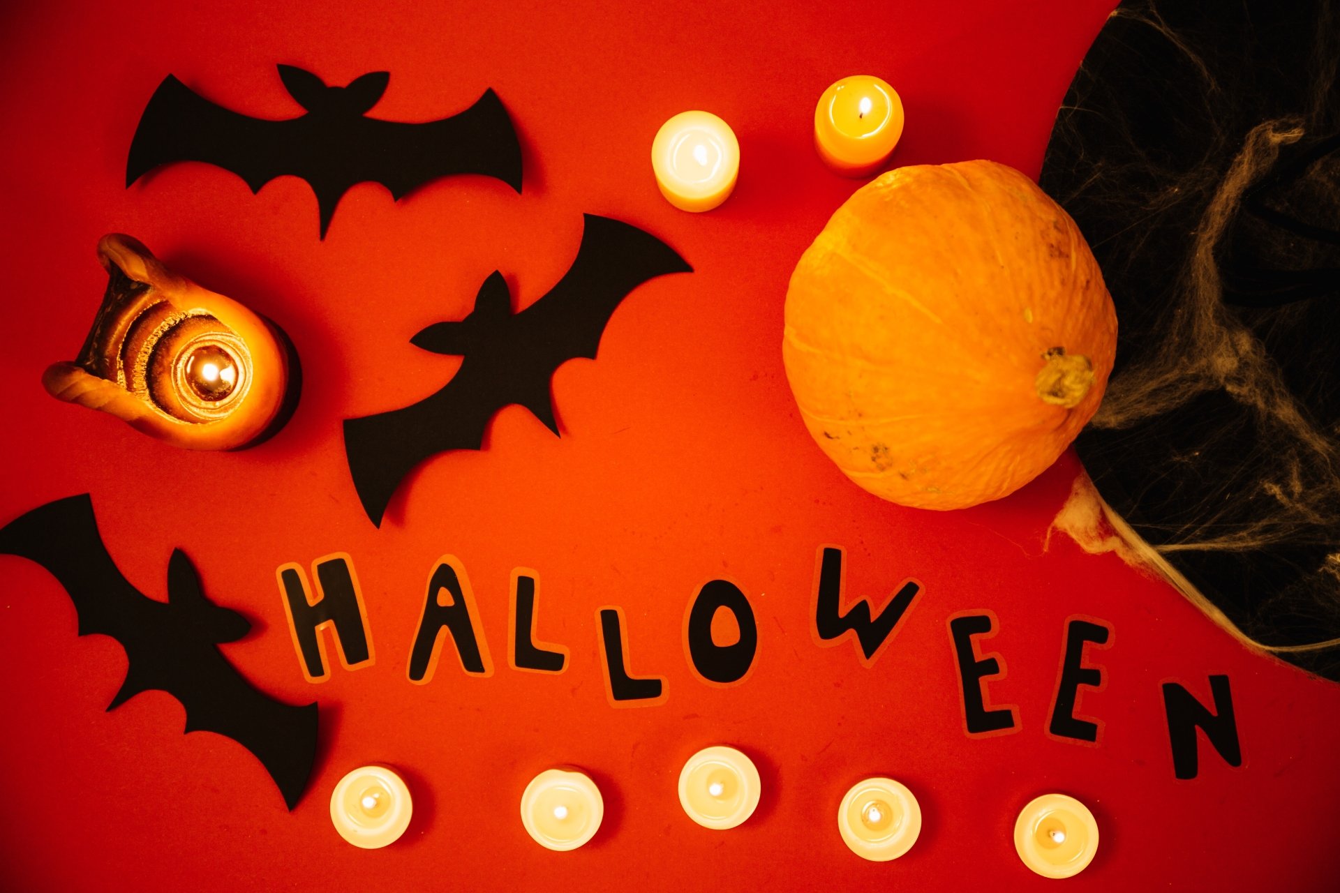 4K Ultra HD Halloween desktop wallpaper featuring bats, a pumpkin, and glowing candles on a vibrant orange background, capturing a spooky holiday atmosphere.