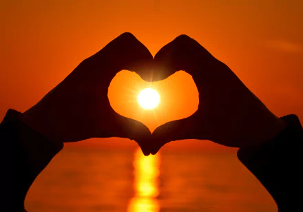 HD desktop wallpaper of a romantic sunset with hands forming a heart shape around the sun, symbolizing love.