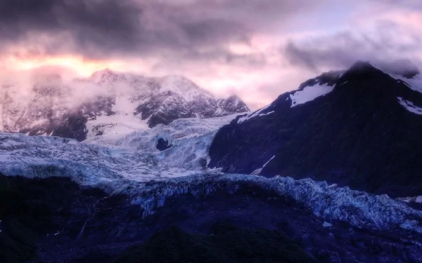 A stunning winter landscape featuring snow-covered mountains beneath a dramatic sky, with cold clouds enhancing the serene beauty of nature. High-definition wallpaper for desktop backgrounds.