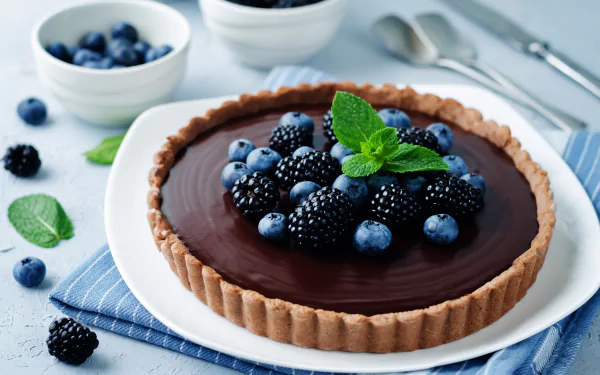 4K Ultra HD image of a chocolate tart topped with fresh blueberries, blackberries, and a mint garnish, styled as a still life food wallpaper background.