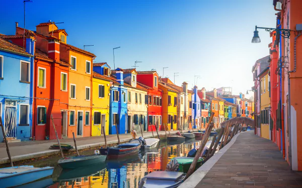 Colorful houses line a canal in Venice, Italy, with gondolas floating peacefully. This vibrant HD wallpaper captures the charm of this iconic city, offering a stunning desktop background.