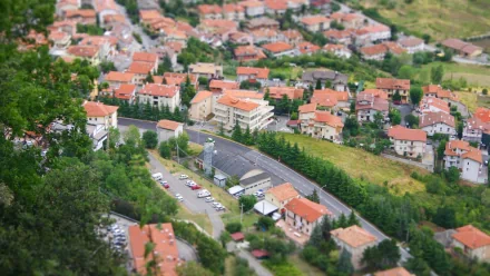 Tilt-shift photography of a village district: landscape of clustered buildings, trees, grass and bushes, with cars along winding streets — HD PC desktop wallpaper/background.