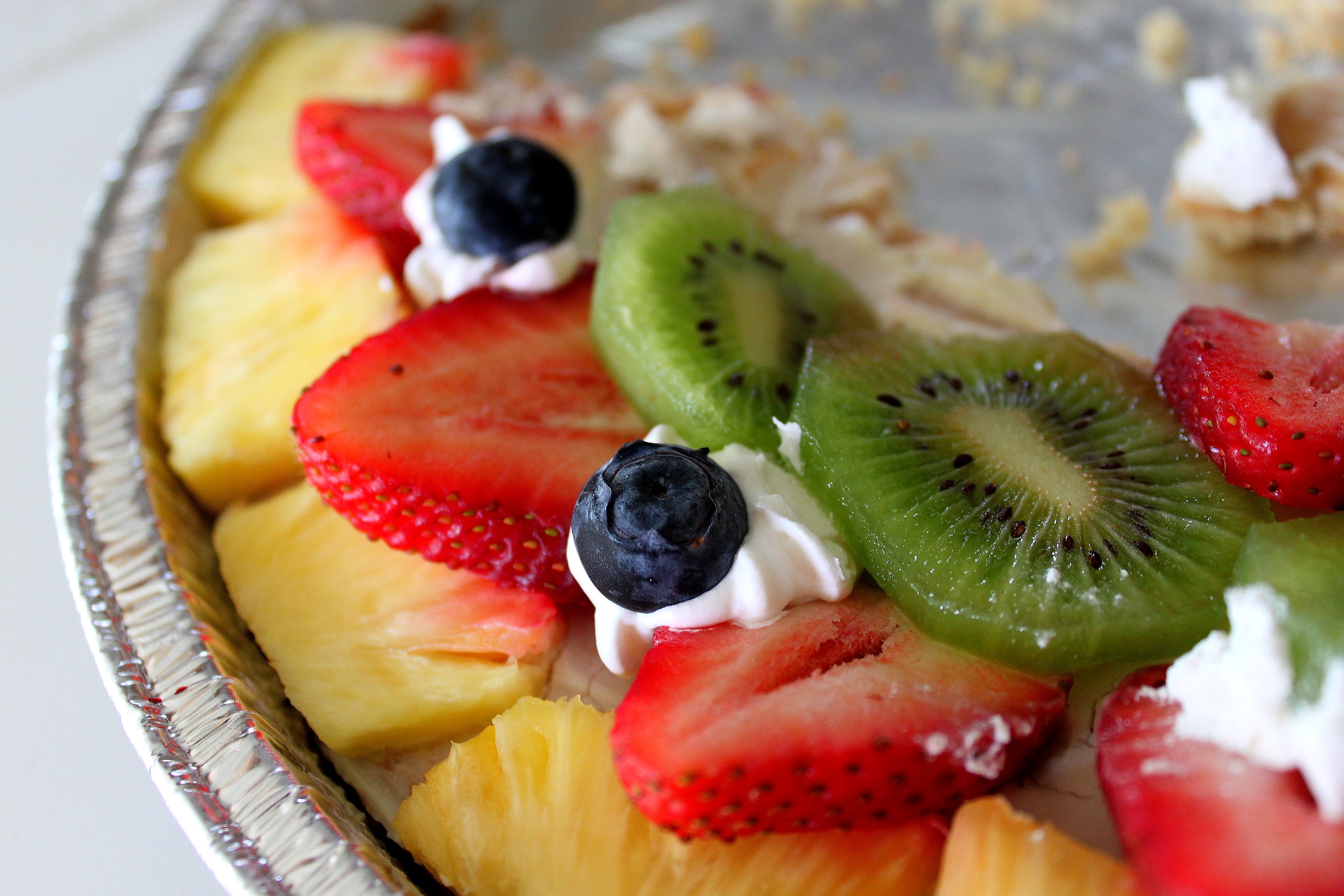 A colorful snack with strawberry, blueberry, pineapple, pie, cream, kiwi, and sugar.