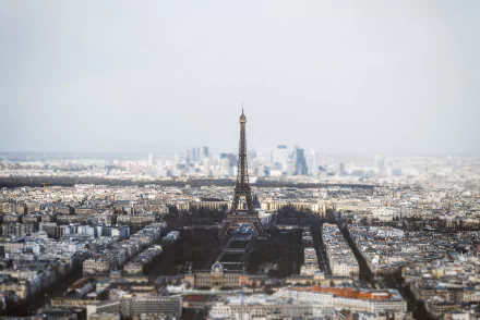 Tilt-shift aerial cityscape of Paris featuring the Eiffel Tower prominently against the horizon, showcasing man-made buildings in a clear HD desktop wallpaper background.