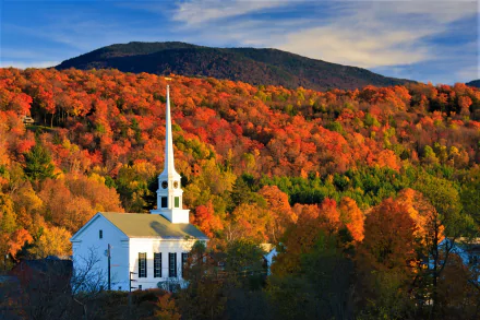 HD PC desktop wallpaper: white church with tall steeple nestled in a colorful fall forest below a mountain, vibrant autumn foliage fills the scene.