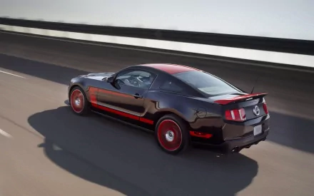 HD desktop wallpaper featuring a Ford Mustang Boss 302 in motion on a highway. The sleek black vehicle with red accents and rims showcases its powerful and stylish design against a blurred background.