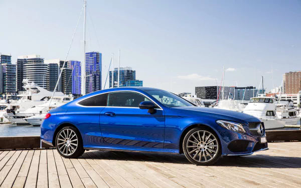 Blue Mercedes‑Benz C‑Class coupe parked on a wooden marina pier with yachts and city skyline in the background — 4K Ultra HD PC desktop wallpaper.