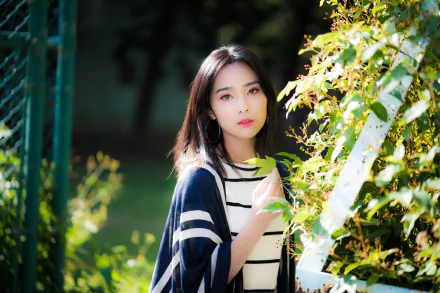 HD desktop wallpaper featuring a poised brunette Asian woman in a striped outfit, accentuated by a natural background and focused depth of field.
