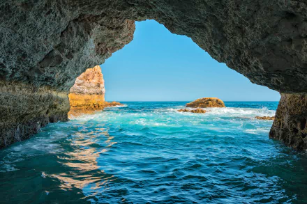 HD desktop wallpaper of a stunning ocean view through a natural sea cave in Portugal, capturing the horizon and serene blue waters.
