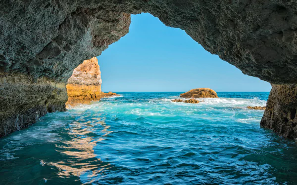 HD desktop wallpaper of a stunning ocean view through a natural sea cave in Portugal, capturing the horizon and serene blue waters.