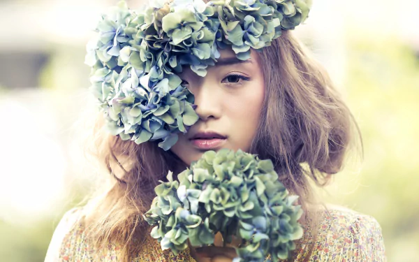 5K Ultra HD PC Desktop Wallpaper and Background: close-up of a brunette woman model wearing a floral wreath, hydrangea blooms partially covering her face, soft-focus natural backdrop.
