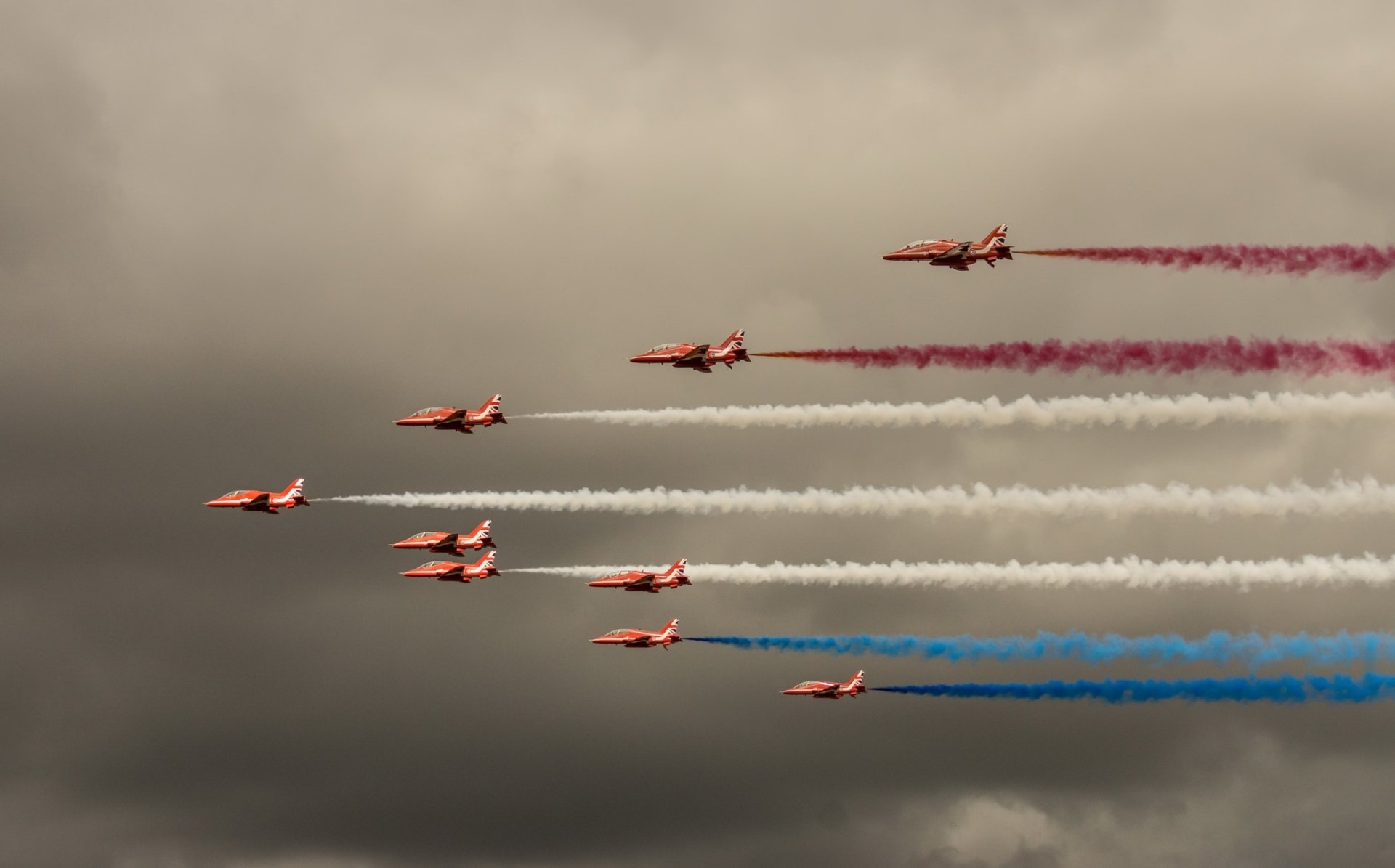 A formation of jet fighter aircraft releases colorful smoke trails during a military air show, captured as a striking HD desktop wallpaper and background.
