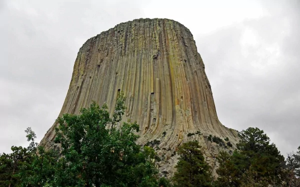 HD desktop wallpaper showcasing Devils Tower, a striking natural mountain formation rising above lush green trees under a cloudy sky.
