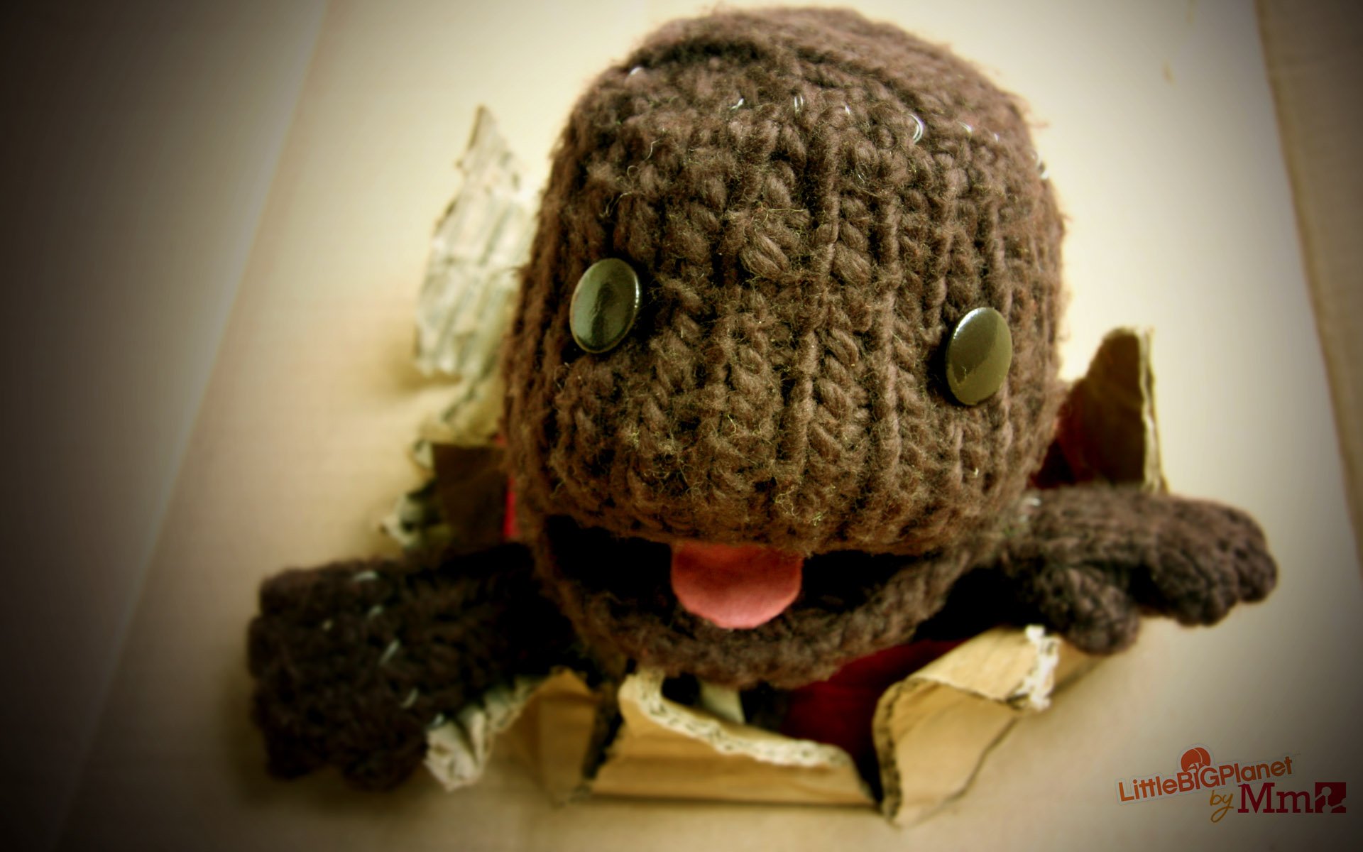 HD PC desktop wallpaper featuring Sackboy, the knitted character from the video game LittleBigPlanet, emerging from a torn surface with a playful expression.