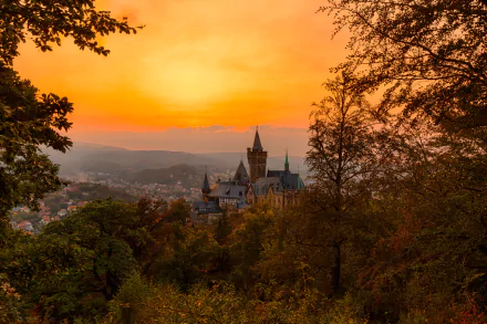 HD desktop wallpaper showing a stunning sunset over a German castle, surrounded by lush trees and a serene landscape. The warm hues of the setting sun create a captivating background.