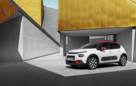 White Citroën C3 car parked in front of modern architecture with gold and gray geometric walls, captured in a high-definition desktop wallpaper background.