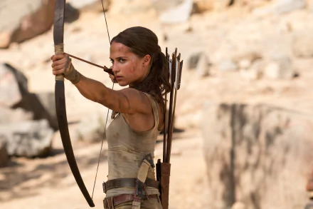 Alicia Vikander as Lara Croft in Tomb Raider (2018), aiming a bow and arrow in a desert setting. This HD desktop wallpaper captures the intense, action-packed essence of the movie.