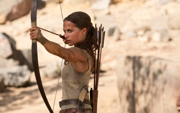 Alicia Vikander as Lara Croft in Tomb Raider (2018), aiming a bow and arrow in a desert setting. This HD desktop wallpaper captures the intense, action-packed essence of the movie.