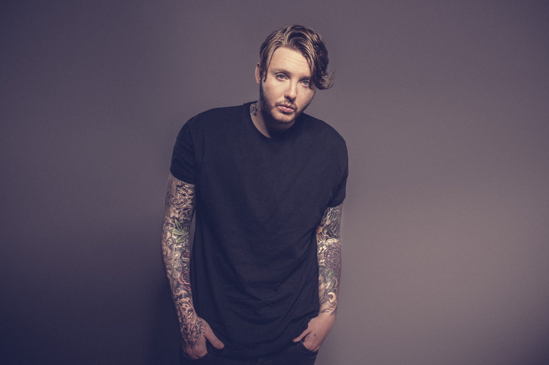 Man with sleeve tattoos in a black t-shirt posing for an HD desktop wallpaper.