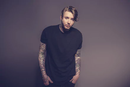 Man with sleeve tattoos in a black t-shirt posing for an HD desktop wallpaper.