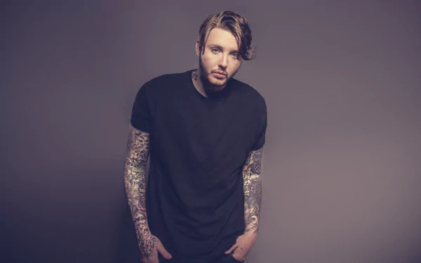 Man with sleeve tattoos in a black t-shirt posing for an HD desktop wallpaper.