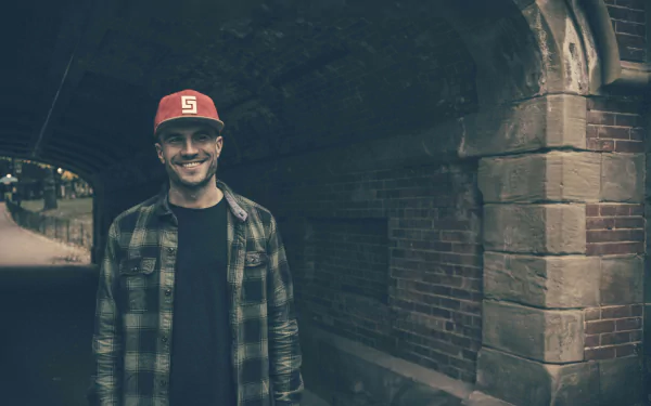 Man in a plaid shirt and red cap smiling under a bridge, HD desktop wallpaper background.
