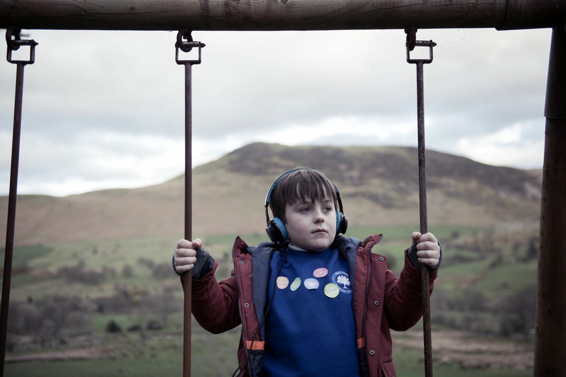 HD desktop wallpaper from The A Word featuring a young boy on a swing with a scenic backdrop of hills.