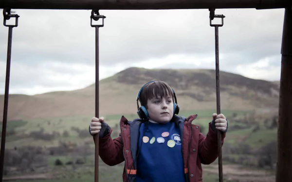 HD desktop wallpaper from The A Word featuring a young boy on a swing with a scenic backdrop of hills.