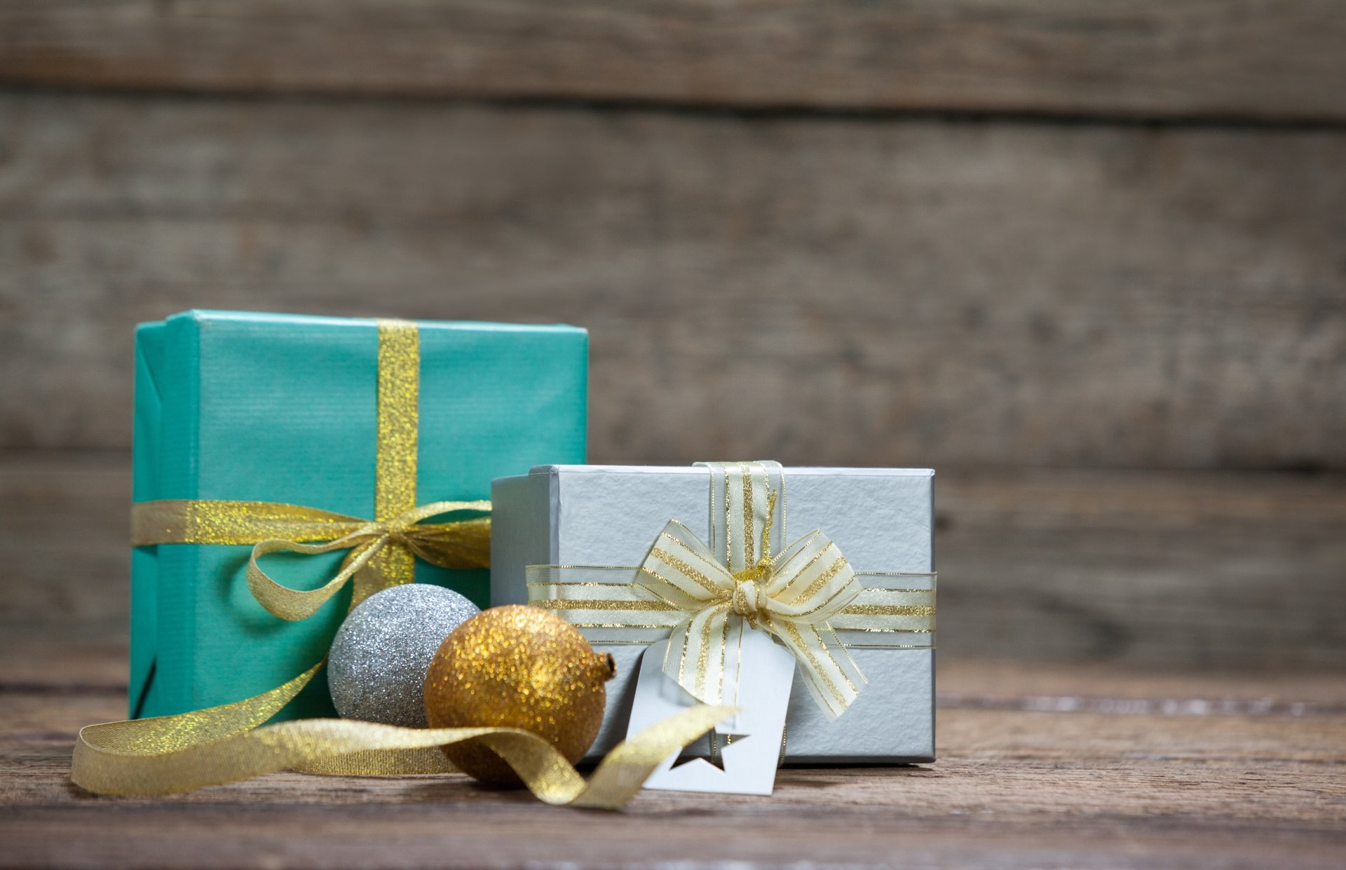 Two elegantly wrapped gift boxes with gold ribbons and decorative baubles on a wooden surface, captured in crisp 4K Ultra HD detail for PC desktop wallpaper.