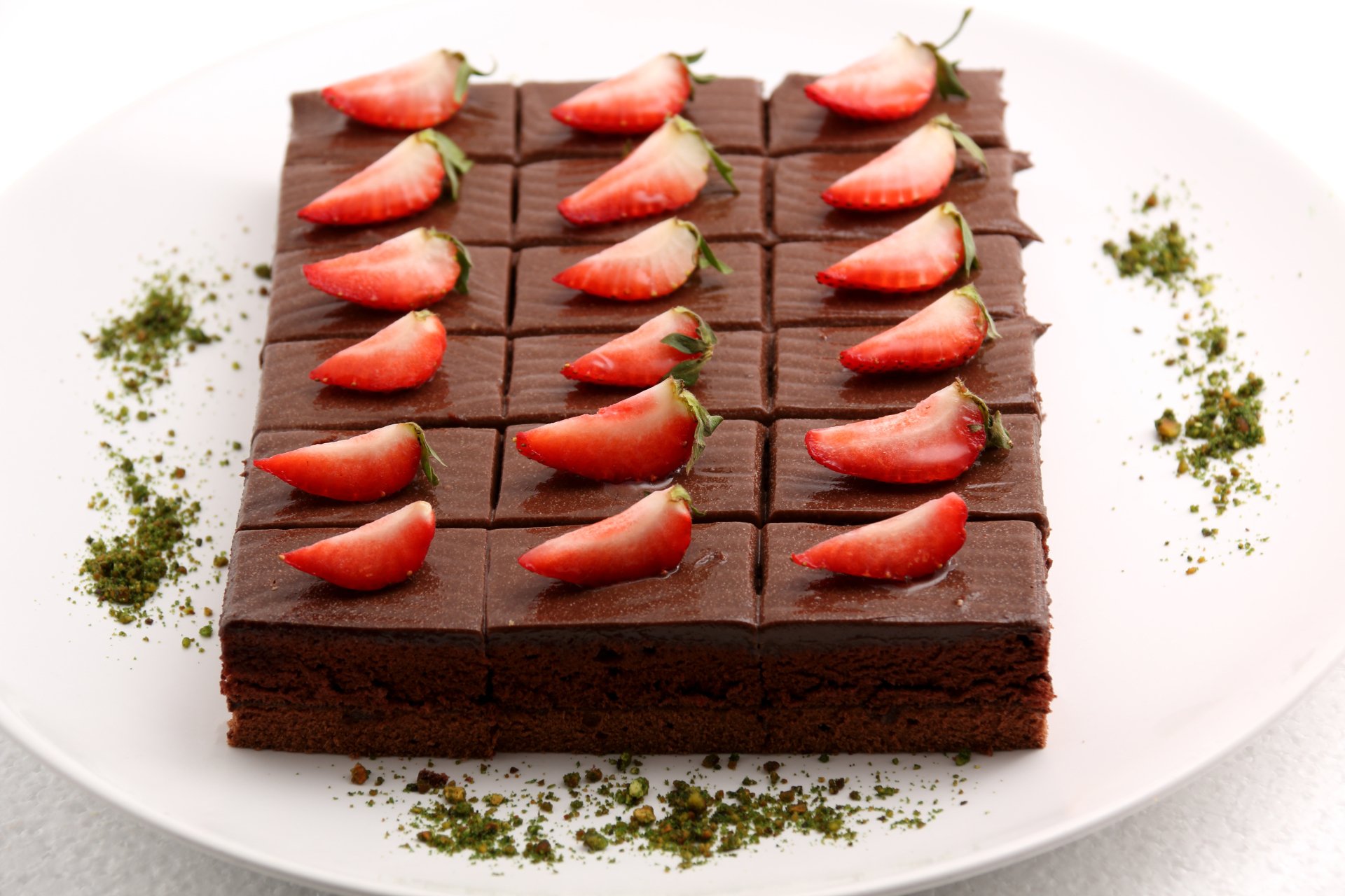 5K Ultra HD PC desktop wallpaper and background: rich chocolate brownie dessert topped with sliced strawberries arranged in rows on a white plate, garnished with green crumbs.