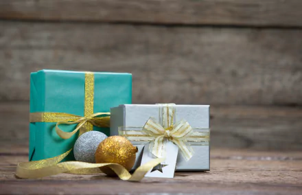 Two elegantly wrapped gift boxes with gold ribbons and decorative baubles on a wooden surface, captured in crisp 4K Ultra HD detail for PC desktop wallpaper.