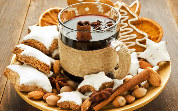 HD desktop wallpaper featuring cinnamon sticks, gingerbread cookies, star-shaped iced cookies, dried orange slices, and a glass of dark spiced drink on a wooden table.