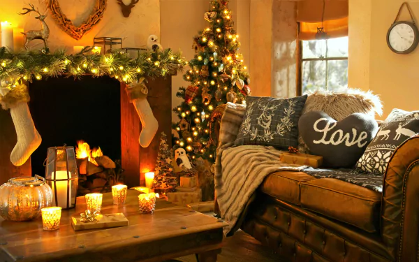A cozy living room decorated for Christmas with a fireplace, stockings, and a Christmas tree. A sofa with holiday-themed pillows and a table with candles add warmth to the festive scene. HD desktop wallpaper.