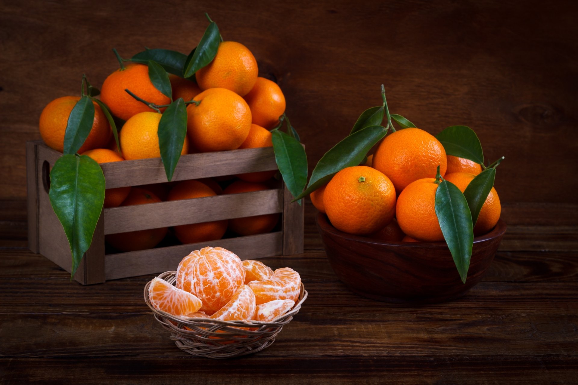 Still life of fresh mandarins with green leaves in a wooden crate, a bowl, and peeled segments in a glass dish, captured in stunning 4K Ultra HD quality.
