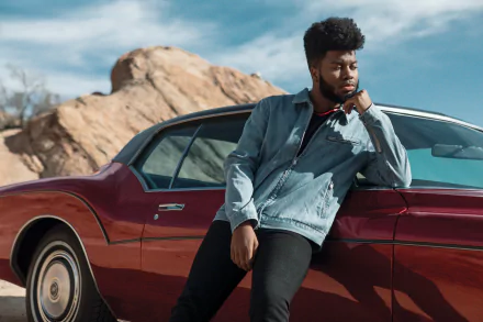 HD desktop wallpaper of a person leaning on a classic red car with a rocky landscape in the background, tagged with Khalid.