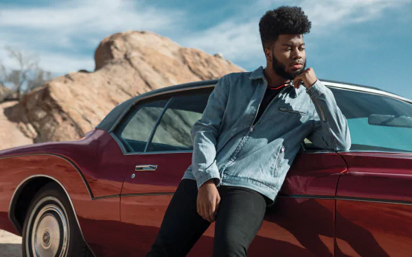 HD desktop wallpaper of a person leaning on a classic red car with a rocky landscape in the background, tagged with Khalid.