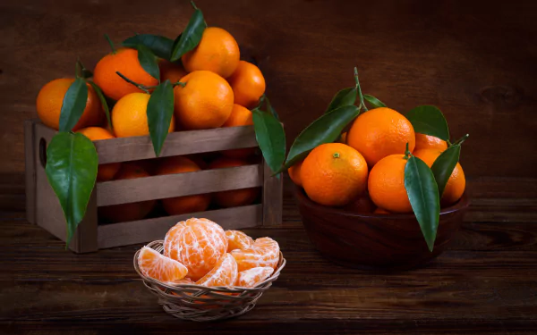 Still life of fresh mandarins with green leaves in a wooden crate, a bowl, and peeled segments in a glass dish, captured in stunning 4K Ultra HD quality.