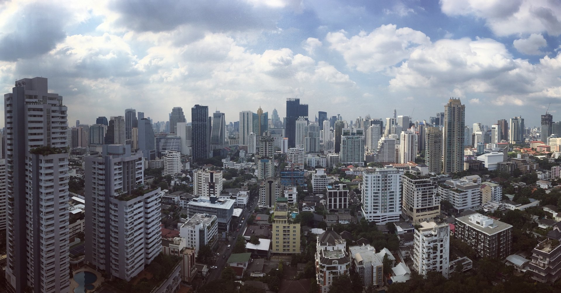 2K Quad HD PC desktop wallpaper: Bangkok man-made skyline beneath dramatic clouds, dense high-rise cityscape.