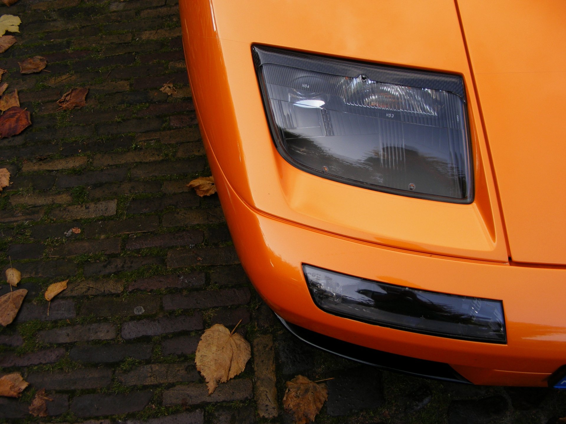 Close-up of orange Lamborghini Diablo front corner and headlight on cobblestones, 2K Quad HD PC desktop wallpaper background