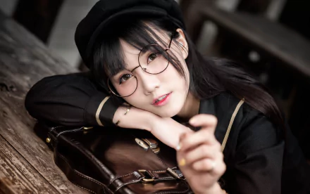 HD desktop wallpaper featuring an Asian brunette woman model wearing glasses and a black beret, posing with a thoughtful expression against a rustic wooden background.