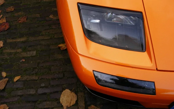 Close-up of orange Lamborghini Diablo front corner and headlight on cobblestones, 2K Quad HD PC desktop wallpaper background
