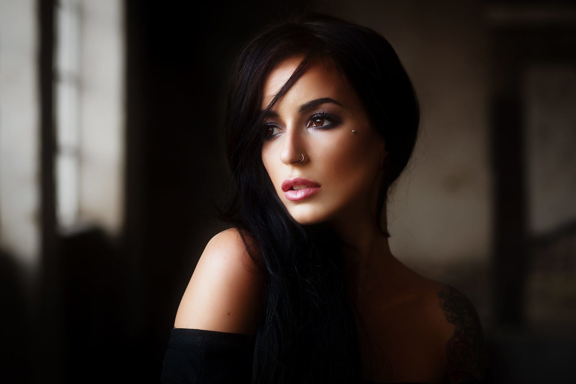 HD PC desktop wallpaper of a brown-eyed woman model with long black hair, off-shoulder top, soft lighting and a moody blurred background.