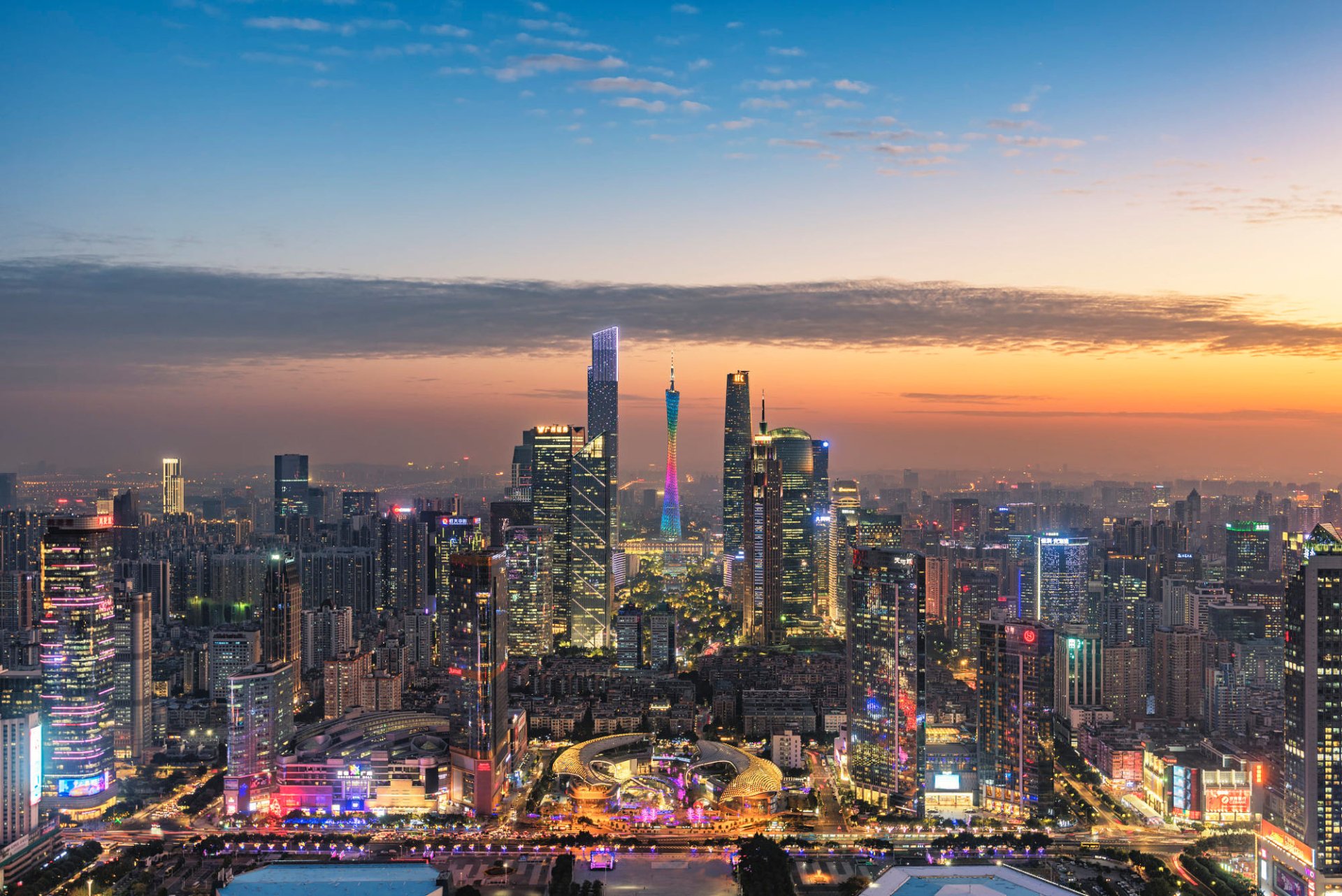HD desktop wallpaper featuring a vibrant cityscape of Guangzhou, China at sunset, with the Canton Tower prominently in the background among other towering buildings.