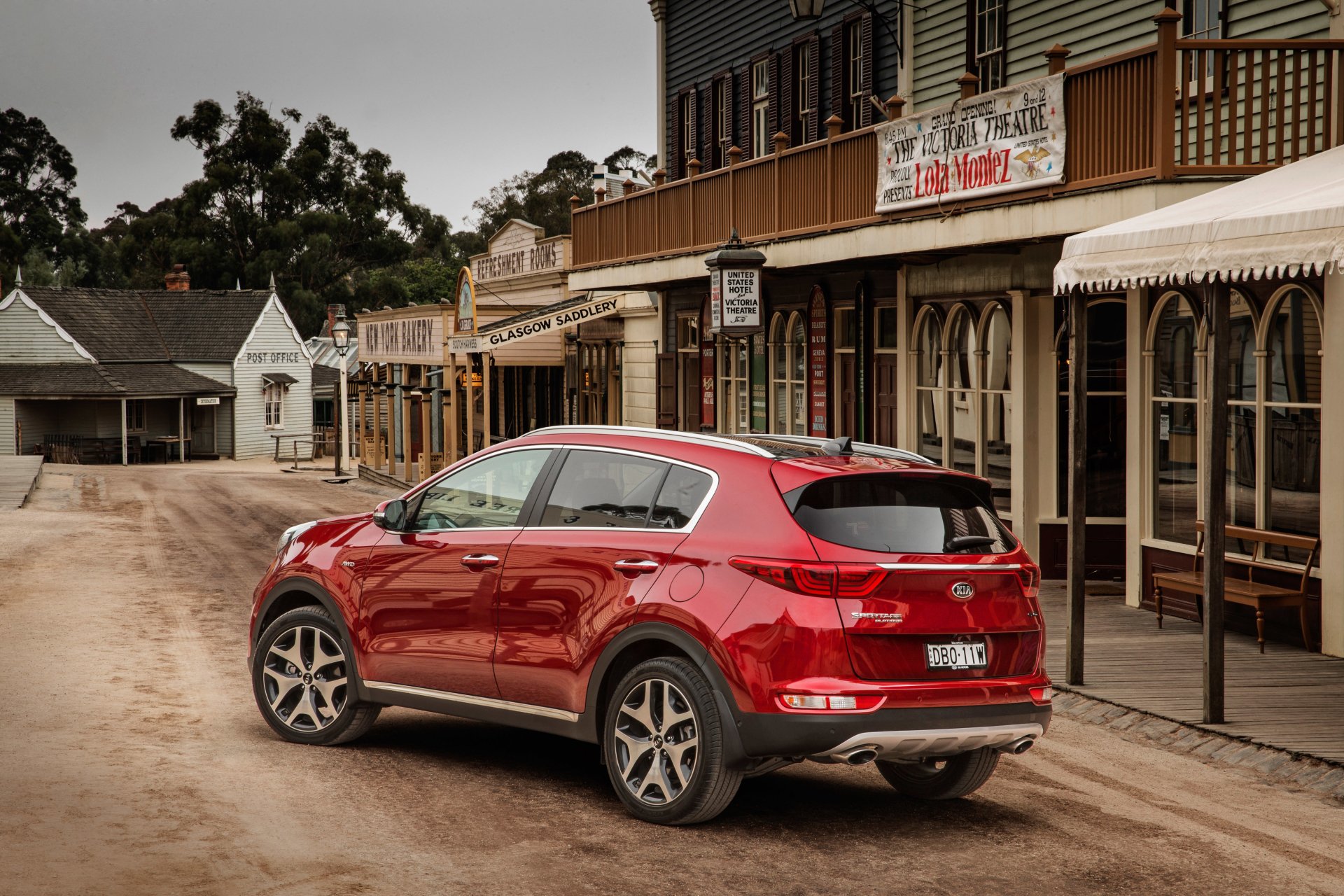 Red Kia Sportage SUV parked on a dusty street in a rustic town, featured as a 4K Ultra HD PC desktop wallpaper and background showcasing the vehicle’s design.